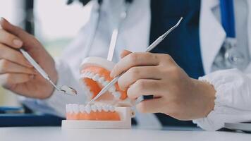 dentista sentado a la mesa con muestras de mandíbula modelo de diente y trabajando con tableta y computadora portátil en el consultorio dental clínica dental profesional. medico trabajando video