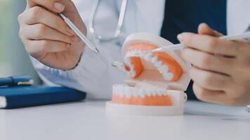 dentista sentado a la mesa con muestras de mandíbula modelo de diente y trabajando con tableta y computadora portátil en el consultorio dental clínica dental profesional. medico trabajando video