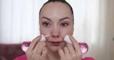 Portrait of attractive woman using facial massage roller and smilling while looking to camera. Female young model with naked shoulders and light nude make up posing .Concept of skincare video