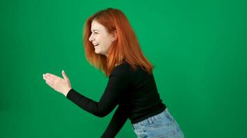 A red-haired girl in black clothes makes dance moves and straightens her hair. green background video