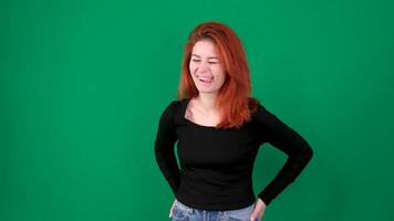 un niña con rojo pelo muecas y sonrisas, demostración diferente emociones en un verde antecedentes. video
