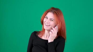 Red-haired girl talking on White phone, smiling, satisfied, happy. Green background. Hand gestures video