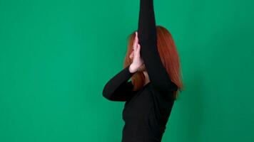 A red-haired girl in black clothes raises her hands up and lowers her hands, stroking her hair. video