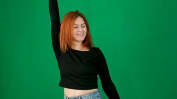 een roodharig meisje in zwart kleren maakt dans beweegt en rechtzetten haar haar. groen achtergrond video