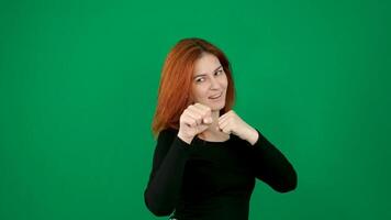 A red-haired girl in black clothes stands in a boxer's stance, smiles and waves her fist. on a green background video