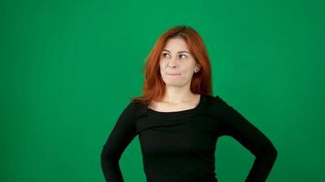 Red-haired girl in black clothes makes faces, shows tongue, smiles with different emotions green background video