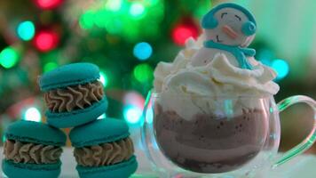 Snowman dessert macaron decorated with hat and scarf with colorful lights and bokeh flashing on foreground and Christmas tree on background. Merry Christmas and Happy New Year festive concept video