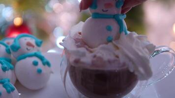 Snowman dessert macaron decorated with hat and scarf with colorful lights and bokeh flashing on foreground and Christmas tree on background. Merry Christmas and Happy New Year festive concept video