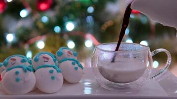 torrencial caliente chocolate dentro Leche en contra el antecedentes de un nuevo años Navidad árbol y un monigote de nieve hecho de merengue postre en Navidad noche cena vaso gotas de delicioso cacao video