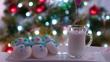 Snowman dessert macaron decorated with hat and scarf with colorful lights and bokeh flashing on foreground and Christmas tree on background. Merry Christmas and Happy New Year festive concept video