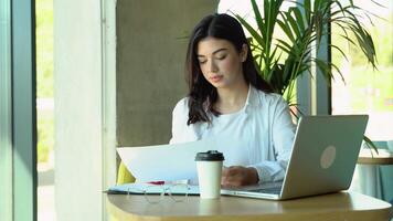 Serious businesswoman using laptop and working with documents. Caucasian insurance agent checking papers and working on computer video