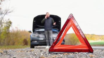 Road side warning triangle, warning oncoming traffic of a broken down car, with a man using his cell phone to call for assistance video