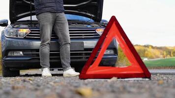 Road side warning triangle, warning oncoming traffic of a broken down car, with a man using his cell phone to call for assistance video