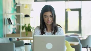 Smiling girl freelancer chatting with client while resting at cafe, using laptop video