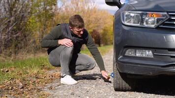 Man lifts car on jack to replace punctured tire. Replacement of punctured tire on road. Help video