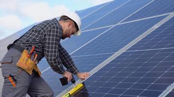 Male engineer in protective helmet installing solar photovoltaic panel system using screwdriver. Alternative energy ecological concept video