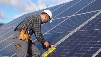 Male engineer in protective helmet installing solar photovoltaic panel system using screwdriver. Alternative energy ecological concept video