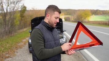 joven hombre preparando un rojo triángulo a advertir otro la carretera usuarios, coche Descompostura o motor fracaso detener a campo calle video