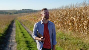 Caucasian farm worker walking along maize corn field for inspection. Harvest care concept video