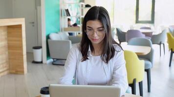 Smiling girl freelancer chatting with client while resting at cafe, using laptop video