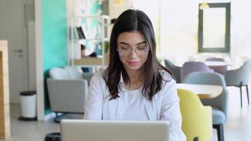 Smiling girl freelancer chatting with client while resting at cafe, using laptop video