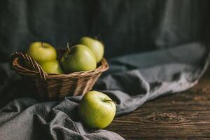 Ripe green apples in a basket on wooden table with cloth. photo