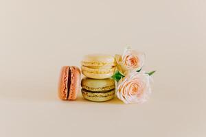 sabroso francés macarons con oferta Rosa flores en un melocotón pastel antecedentes. foto