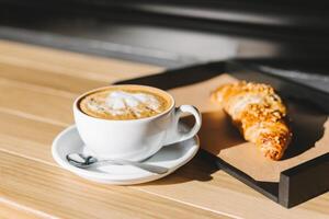 taza de café con francés cuerno para desayuno en un de madera mesa en un al aire libre cafetería. foto