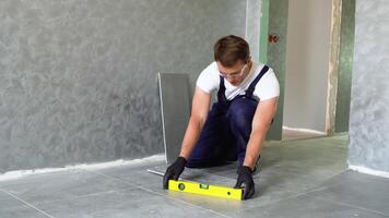 Worker sitting on floor and installing carpenter level on freshly laid tiles in apartment video