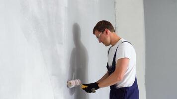 Jeune peintre détient peindre rouleau et La peinture une mur. La peinture intérieur mur avec peindre rouleau dans Nouveau maison. Accueil décoration concept video