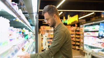 uma homem compras laticínios produtos dentro mercearia loja. lado Visão do bonito homem comprando leite video