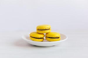 Three yellow french macarons on a white plate and wooden table. Banana macarons with chocolate cream. photo