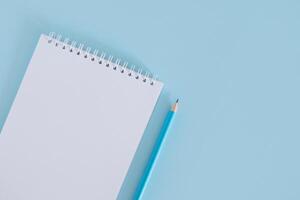 Notebook with blank page and pencil on light blue background. photo