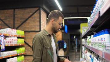 uma homem comprador escolhe xampu ou chuveiro gel dentro supermercado video