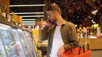 Jeune homme dans une supermarché pourparlers sur le téléphone, consulte avec le sien épouse à propos le achats liste video