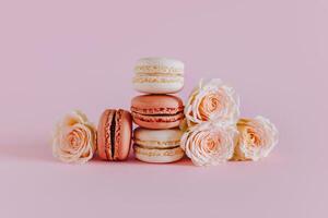 sabroso francés macarons con oferta Rosa flores en un rosado pastel antecedentes. foto