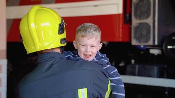 coraggioso pompiere nel uniforme Tenere poco divertente ragazzo contro il sfondo di un' fuoco motore video
