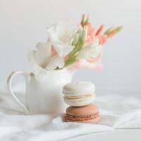 dos pastel francés macarons y flores en un tarro en un blanco antecedentes. foto