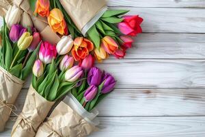 Beautiful bouquets of multicolored tulips wrapped in a craft paper on a white wooden table. photo