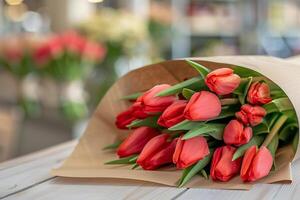 ramo de flores de rojo tulipanes envuelto en un arte papel en un blanco de madera mesa. borroso moderno flor tienda en un antecedentes. foto