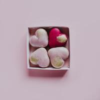 sabroso corazón conformado francés macarons en un caja en un rosado pastel antecedentes. foto