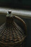 Vintage wicker wine bottle near the window. photo