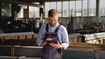 Professional heavy industry engineer worker wearing safety uniform uses tablet computer. Smiling caucasian industrial specialist standing in a metal construction manufacture video