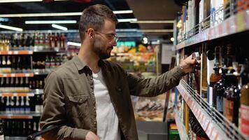 een jong Mens in een supermarkt kiest luxe alcohol in de wijn sectie video