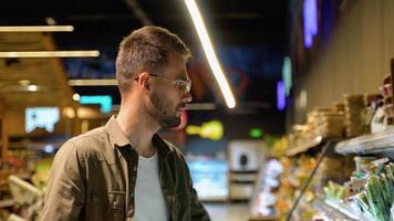 Jeune homme achats dans épicerie magasin. côté vue de concentré homme en portant achats paniers et choisir Frais des légumes dans supermarché. achats concept video