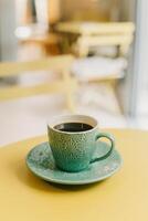 taza de negro café en turquesa cerámico taza en un amarillo mesa en un cafetería. foto