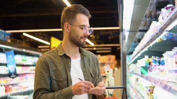 Man writing in his notepad in aisle at supermarket. A man makes notes in the shopping list video