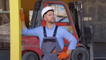 portret van professioneel zwaar industrie ingenieur arbeider vervelend uniform en helm tegen de achtergrond van de magazijn lader video