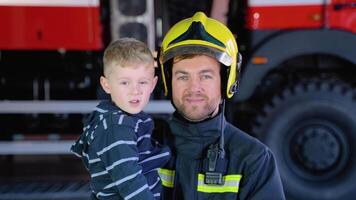 mutig Feuerwehrmann im Uniform halten wenig Junge gegen das Hintergrund von ein Feuer Motor video