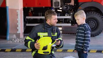 Little boy with firefighter in protective uniform in fire station. Concept of saving lives, fire safety video